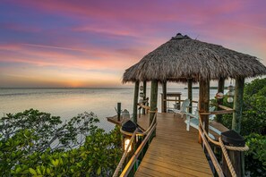 A wooden deck with a thatched-roof structure, chairs, and a view of the sea. - Peninsula Villa Heated Pool Sunset Point (Islamorada)