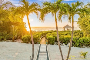 A pathway leading to a beach with palm trees and a thatched structure. - Peninsula Villa Heated Pool Sunset Point (Islamorada)