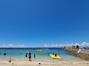 Une plage avec une eau d’un bleu limpide, des gens qui se baignent et des planches de surf.