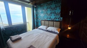 Un letto con testiera, una finestra vista mare e un parete con motivo floreale.
