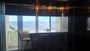 Une pièce avec vue sur l’océan, une table avec des chaises et trois lanternes suspendues.