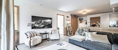 A modern living room with a grey sofa, a white armchair, a small table, and a large black-and-white mountain painting.
