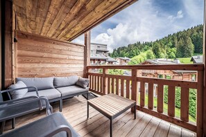 Eine Holzterrasse mit einer Sitzecke, einem Tisch und Blick auf ein bewaldetes Gebiet.