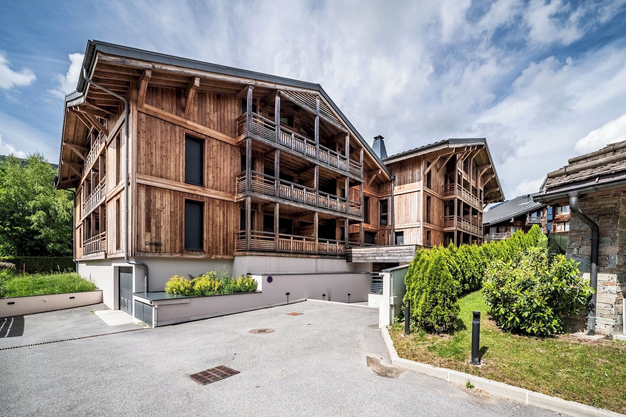 Un edificio de madera de varios pisos con balcones, un acceso empedrado y un jardín ajardinado.