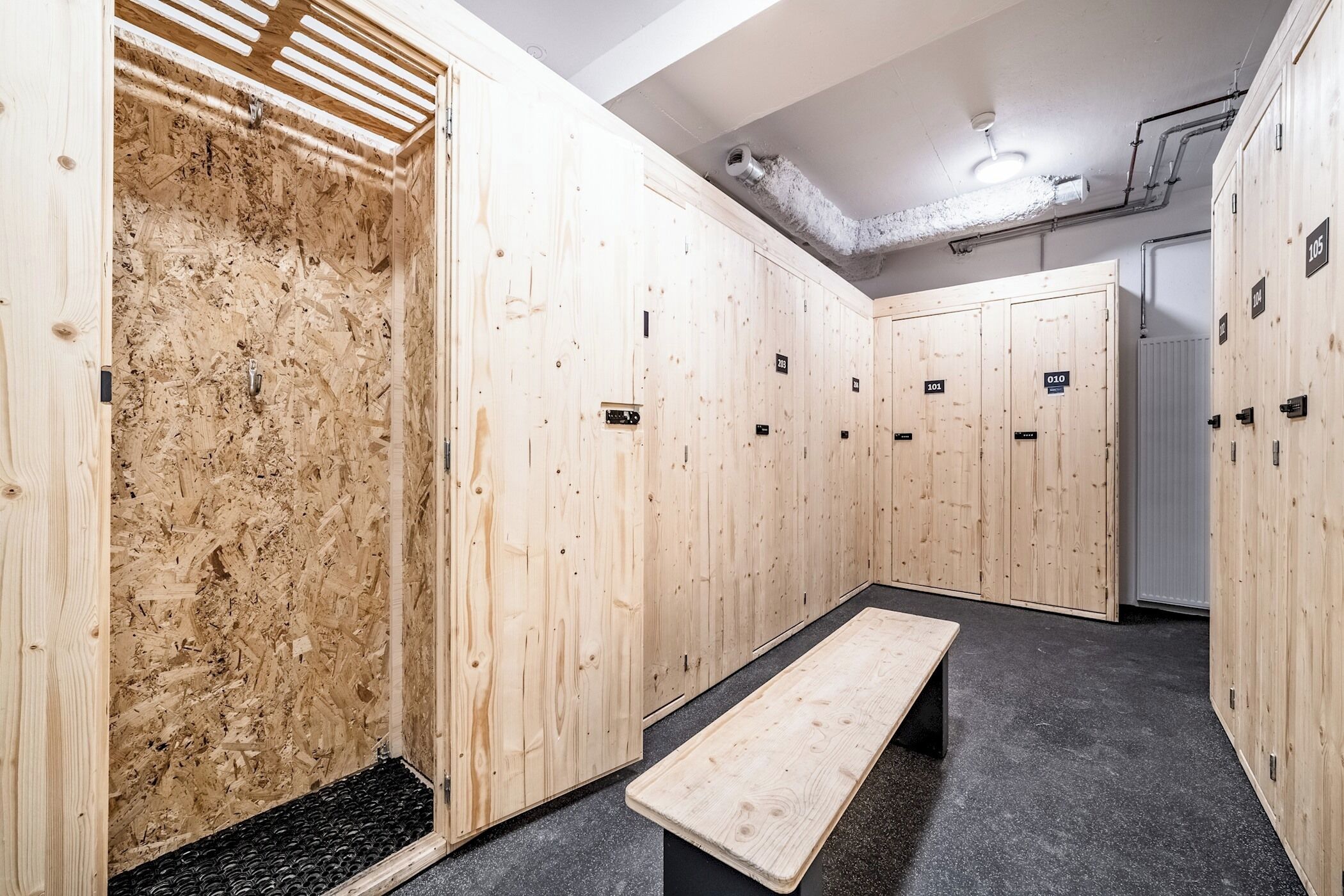 En rad med träskåp, numrerade, en bänk och ett ventilationsgaller i taket.
