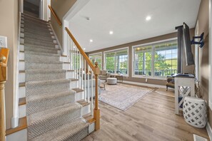 A staircase with carpeted steps and wooden handrails, a large window with a view of greenery, and a white wall-mounted television.