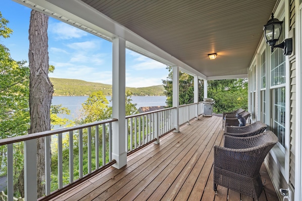 Une véranda couverte donnant sur un lac, une terrasse en bois, des balustrades blanches et des meubles en osier.
