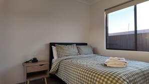 A bedroom with a bed, a nightstand, a lamp, and a window. - Eden Haven  - Cozy Home In Wellard Near Train Station & Rockingham Beach (Wellard)