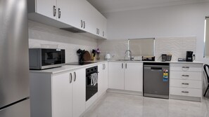 A modern kitchen with white cabinets, stainless steel appliances, and a dishwasher. - Eden Haven  - Cozy Home In Wellard Near Train Station & Rockingham Beach (Wellard)