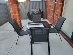Ulkoterassi, jossa on pöytä ja neljä tuolia, grilli ja tiiliseinä.