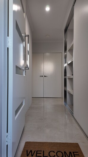 A hallway with a 'WELCOME' mat, a door with a mirror, and a closet with shelves. - Eden Haven  - Cozy Home In Wellard Near Train Station & Rockingham Beach (Wellard)