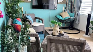 Ein Wohnzimmer mit Rattanmöbeln, einem Flachbildfernseher und Zimmerpflanzen.
