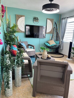A living room with wicker furniture, a flat-screen TV, and decorative plants.
