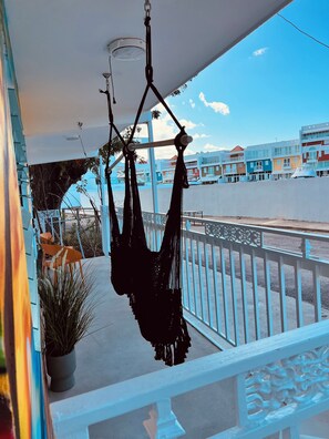 A balcony with a hammock, a potted plant, and a view of colorful buildings.