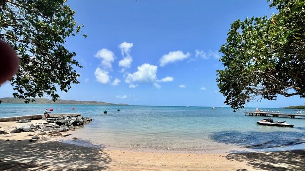 Ein Strand mit klarem Wasser, einer Mole und Booten.