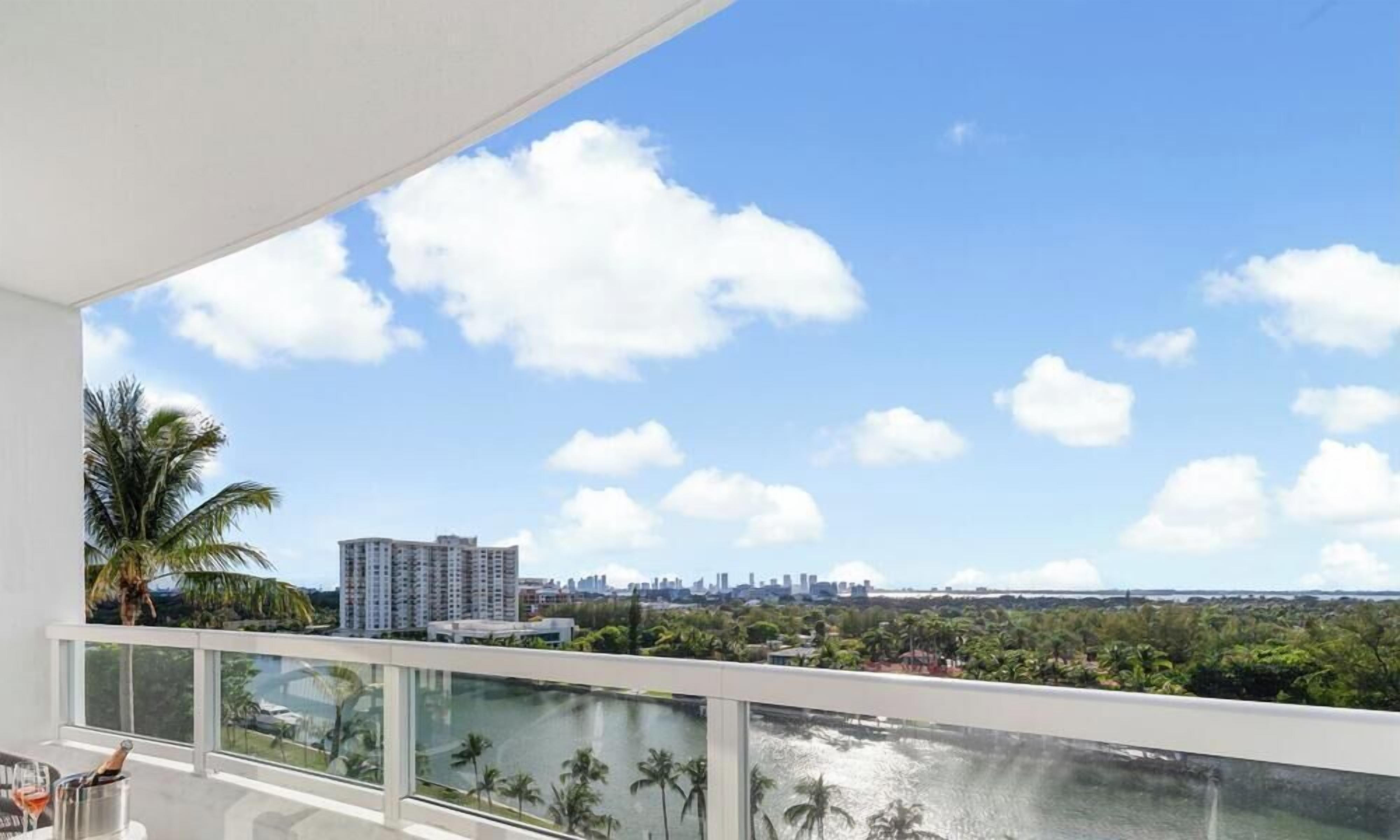 A balcony with a view of a city skyline, palm trees, and a body of water.