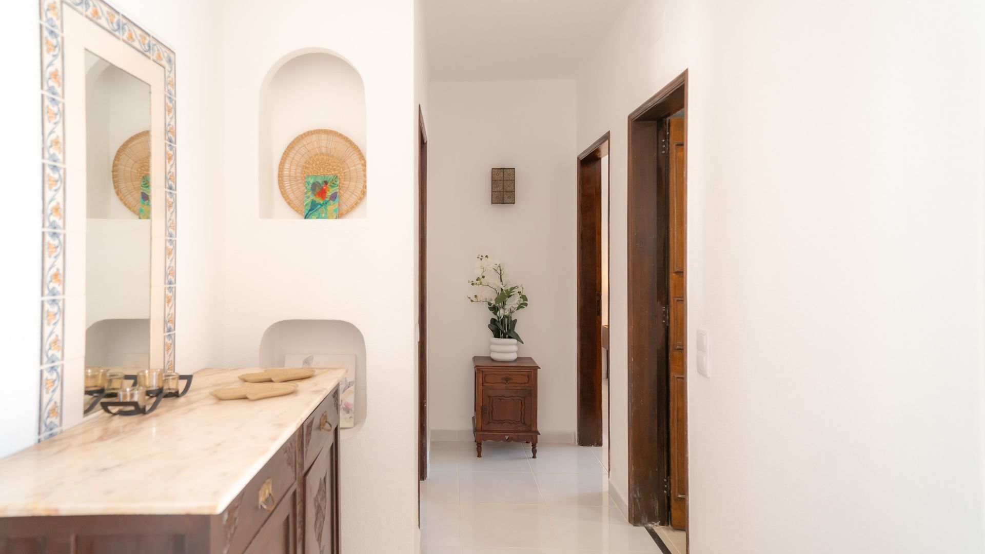 Corredor com balcão de mármore, espelho, pequeno armário e um vaso de flores, além de uma porta.