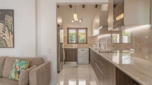 Eine moderne Küche mit einer zentralen Kochinsel, einem Essbereich mit einer Couch und einem großen Fenster für natürliches Licht.