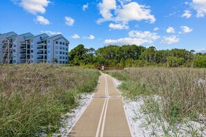A pathway leading to a building with multiple floors, surrounded by natural vegetation and trees. - Folly Field Beach Condo | Pool, Tennis & Gym | Walk to Beach | Sleeps 6 | Gated Community (Hilton Head Island)