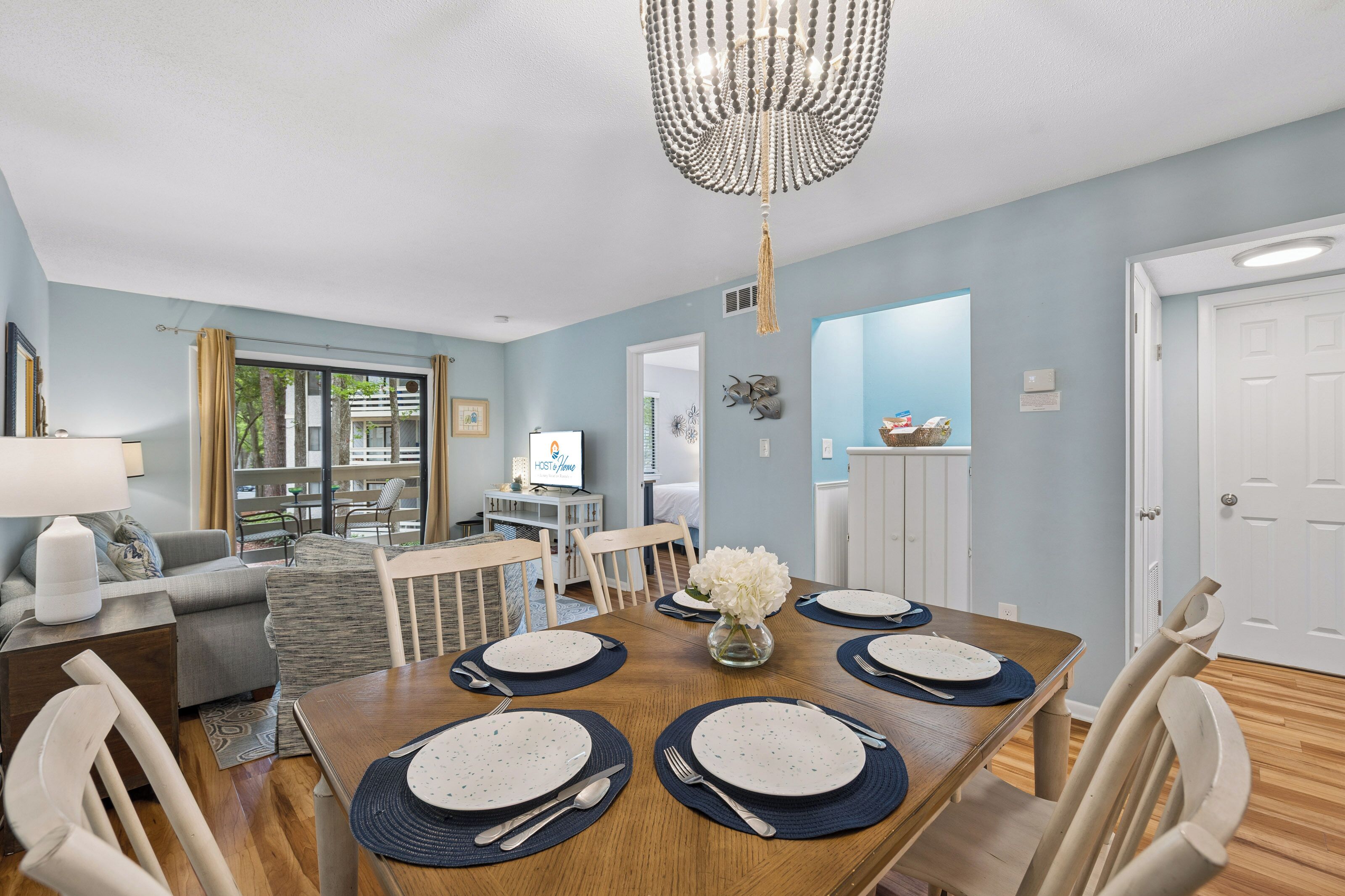 A dining area with a wooden table set for four, a chandelier, and a view of the living room.