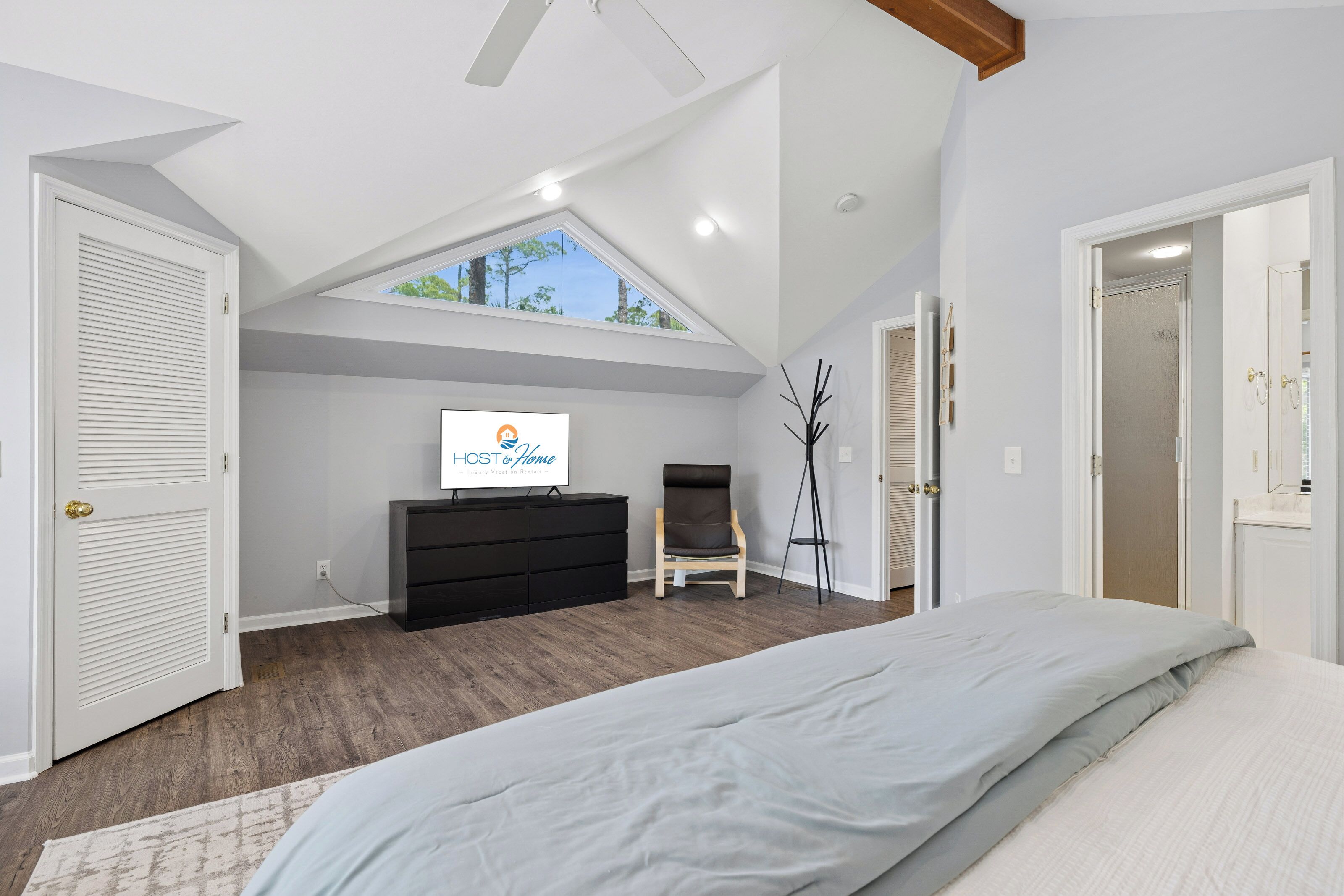 A bedroom with a sloped ceiling, a bed, a dresser, a chair, and a desk with a computer.