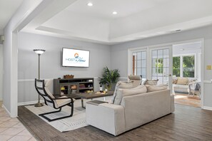 A spacious living room with a sofa, a coffee table, and a TV mounted on the wall. - 5th Row Sea Pines Ocean Escape, Private Pool, Carolina Room, Sleeps 12 (Hilton Head Island)