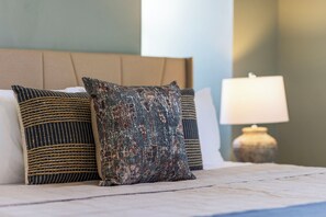 Un lit avec des coussins à motifs, une lampe de chevet et une tête de lit.
