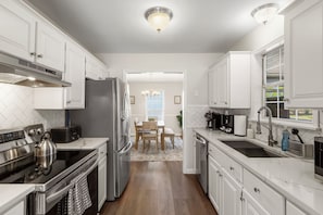 A kitchen with white cabinets, stainless steel appliances, a dining area with a table and chairs, and a view into another room.