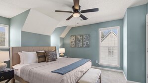 Une chambre à coucher comprenant un lit, un ventilateur de plafond, une table de chevet, un banc et une fenêtre avec des stores.