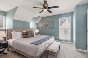 A bedroom with a bed, a ceiling fan, a nightstand, a bench, and a window with blinds.