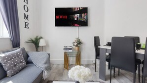 Una sala de estar moderna con un sofá, una mesa de comedor, un televisor montado en la pared y una mesita auxiliar con un florero.