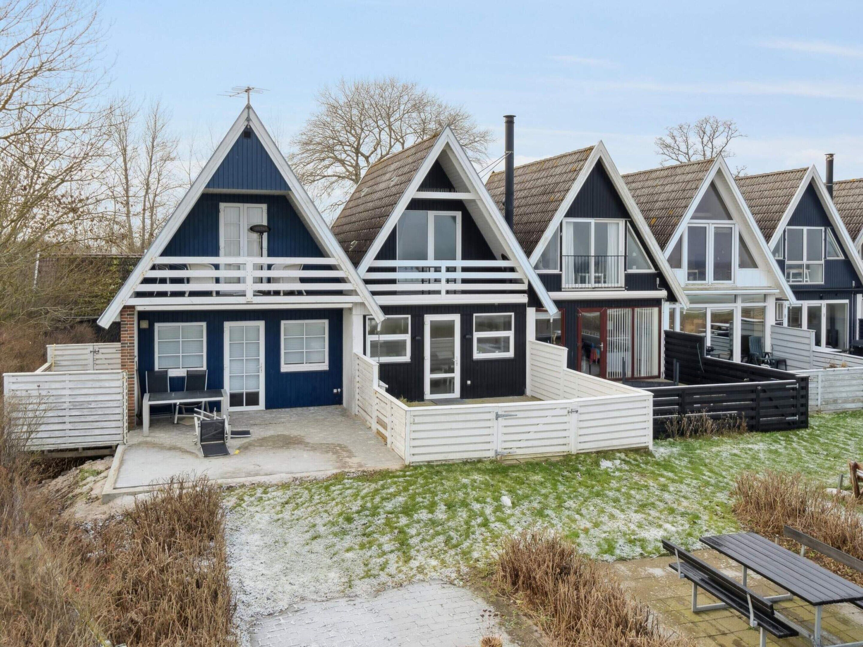 A row of modern, two-story beach houses with white railings, a covered patio, and a gravel path leading to the entrance.