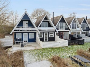 En række moderne sommerhuse med to etager, hvide gelændere, en overdækket terrasse og en grussti, der fører til indgangen.