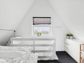 Et soveværelse med seng, et vindue med persienner, et lille skrivebord og en kommode.