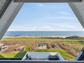 A beach view from a covered area with a white railing, a grassy area with picnic tables, and a sandy beach. - 4 Star Holiday Home in Otterup (Otterup)