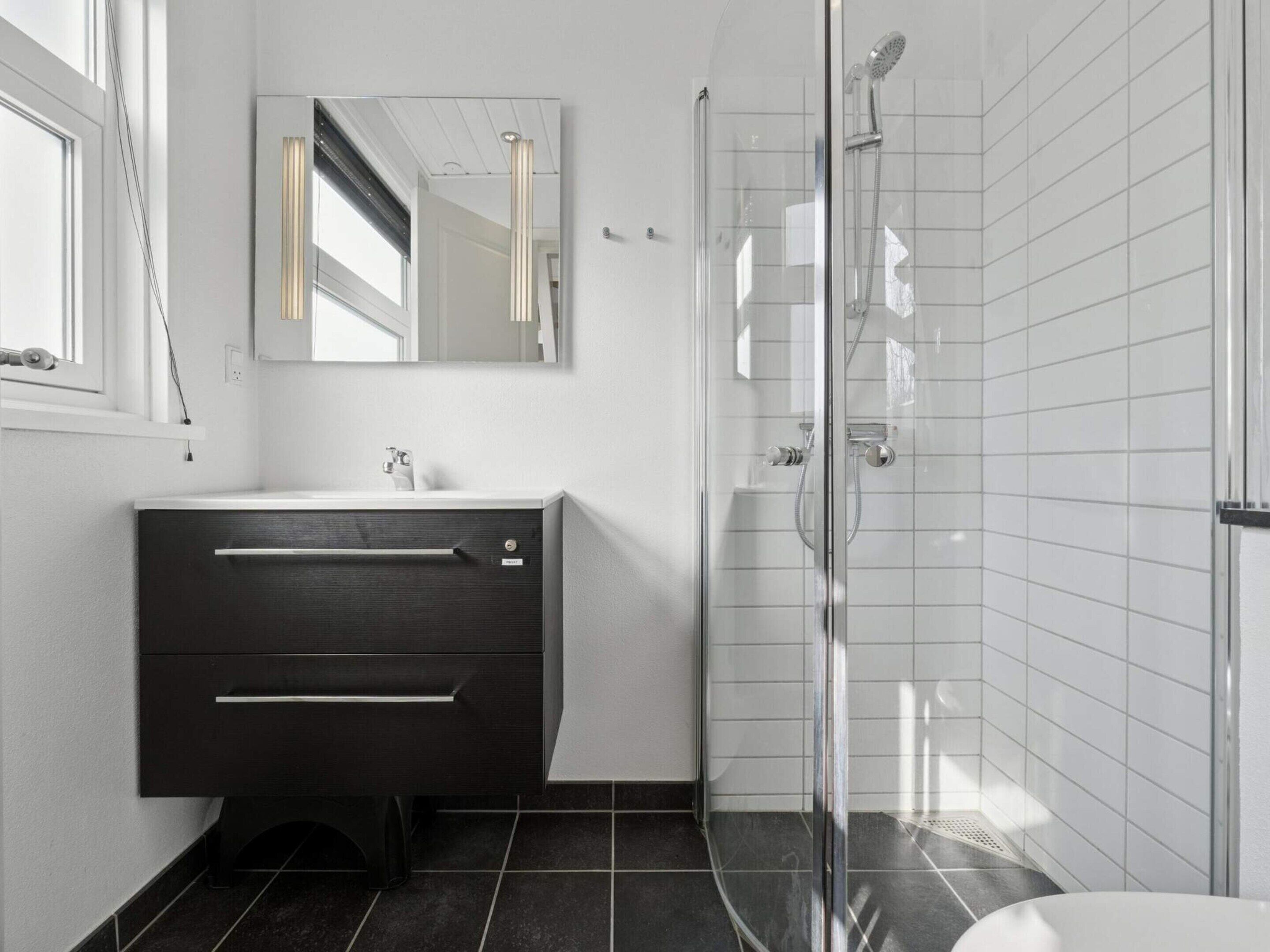 Een moderne badkamer met een donkere wastafelmeubel, een douchecabine met glazen wanden en witte betegelde wanden.