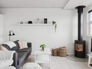 En moderne stue med sofa, et hvidt sofabord, fletkurve, en sort pejs og en hvid væg med hylder.