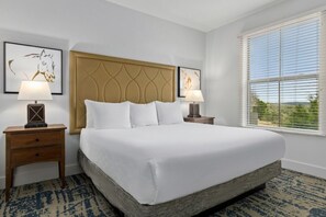 Une chambre d’hôtel avec un grand lit, deux tables de chevet avec des lampes, une tête de lit et des œuvres d’art encadrées accrochées aux murs.