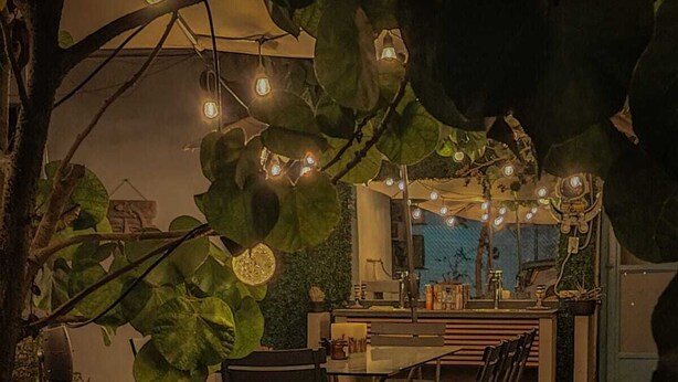 An outdoor dining area with tables and chairs, surrounded by greenery and string lights.