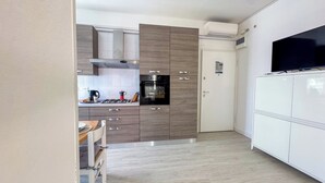 Une cuisine moderne équipée d’un four encastré, d’une machine à café et d’une cuisinière. On y trouve un meuble blanc sur lequel est posé un téléviseur à écran plat.