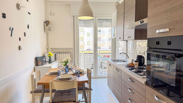Une cuisine compacte dotée d’appareils électroménagers modernes, un coin repas avec une table préparée pour deux personnes, et une vue sur le balcon extérieur.