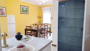Ein Essbereich mit einem Tisch für vier Personen, Stühlen, einem weißen Kühlschrank und einem gerahmten Bild an der Wand.