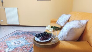 Ein Wohnzimmer mit einer Couch, einem Teppich, einer Schale mit Trauben, einem Glas und einem Blumenstrauß.