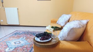 Un soggiorno con divano, un tappeto decorativo, un piatto di uva, un bicchiere e un bouquet di fiori.
