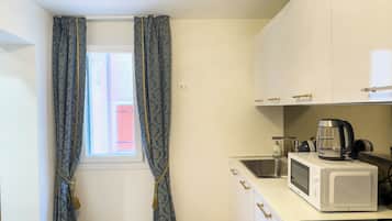 A small kitchen with a window, a sink, a microwave, and a kettle.