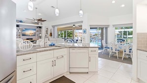 A modern kitchen with white cabinetry, a central island, and a dining area with white chairs. - Fish & Sips - Walking Distance to Cape Harbor - Kayak and Bikes - Intersecting Canal View (Cape Coral)