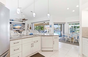 A modern kitchen with white cabinetry, a central island, and a dining area with white chairs. - Fish & Sips - Walking Distance to Cape Harbor - Kayak and Bikes - Intersecting Canal View (Cape Coral)