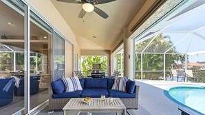 A covered outdoor area with a pool, a blue sofa, and a table with drinks. - Fish & Sips - Walking Distance to Cape Harbor - Kayak and Bikes - Intersecting Canal View (Cape Coral)