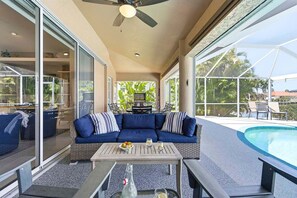 A covered outdoor area with a pool, a blue sofa, and a table with drinks. - Fish & Sips - Walking Distance to Cape Harbor - Kayak and Bikes - Intersecting Canal View (Cape Coral)