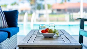 A poolside table with a bowl of fruit, a glass of water, and a glass of beverage. - Fish & Sips - Walking Distance to Cape Harbor - Kayak and Bikes - Intersecting Canal View (Cape Coral)